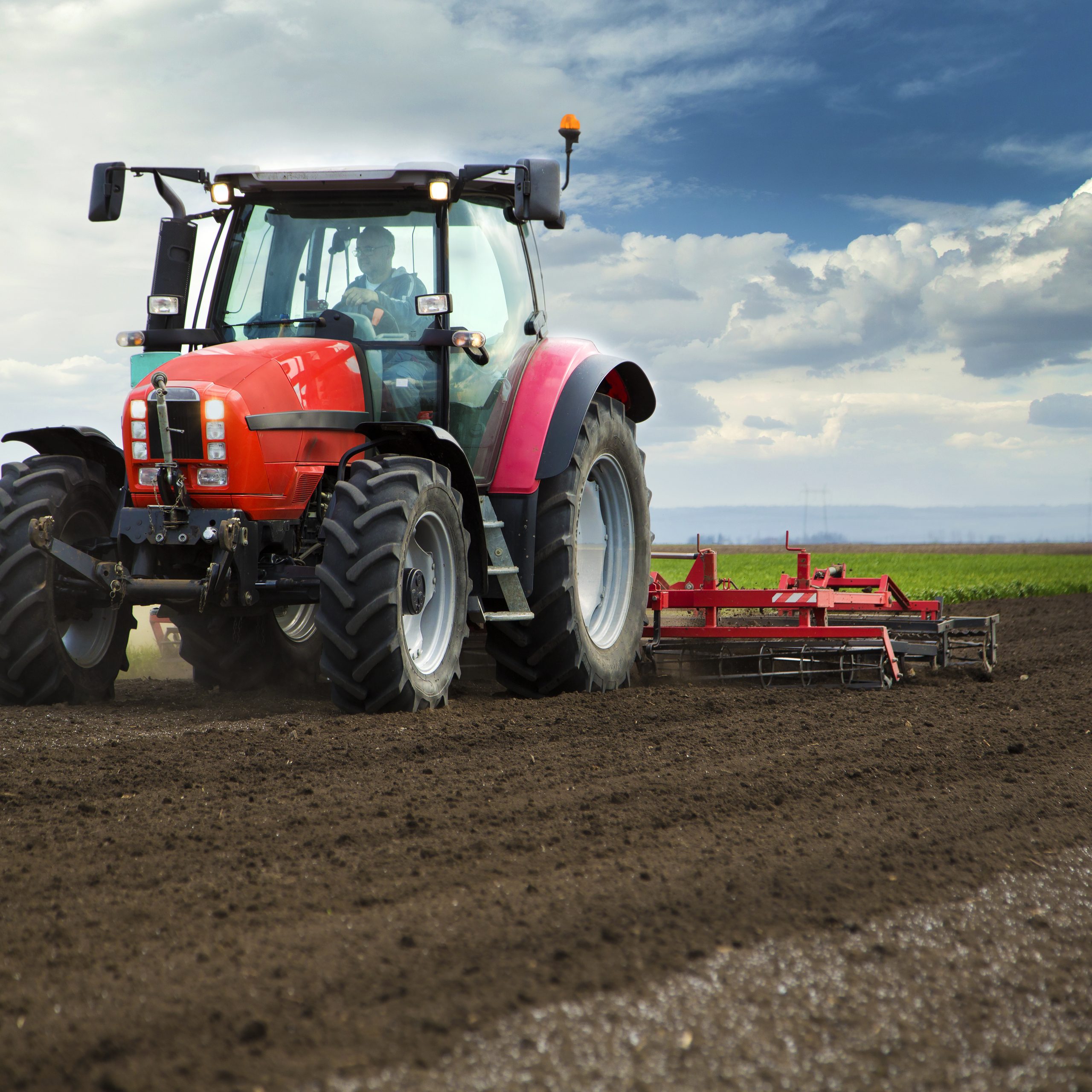Close-up of agriculture red tractor cultivating field over blue sky