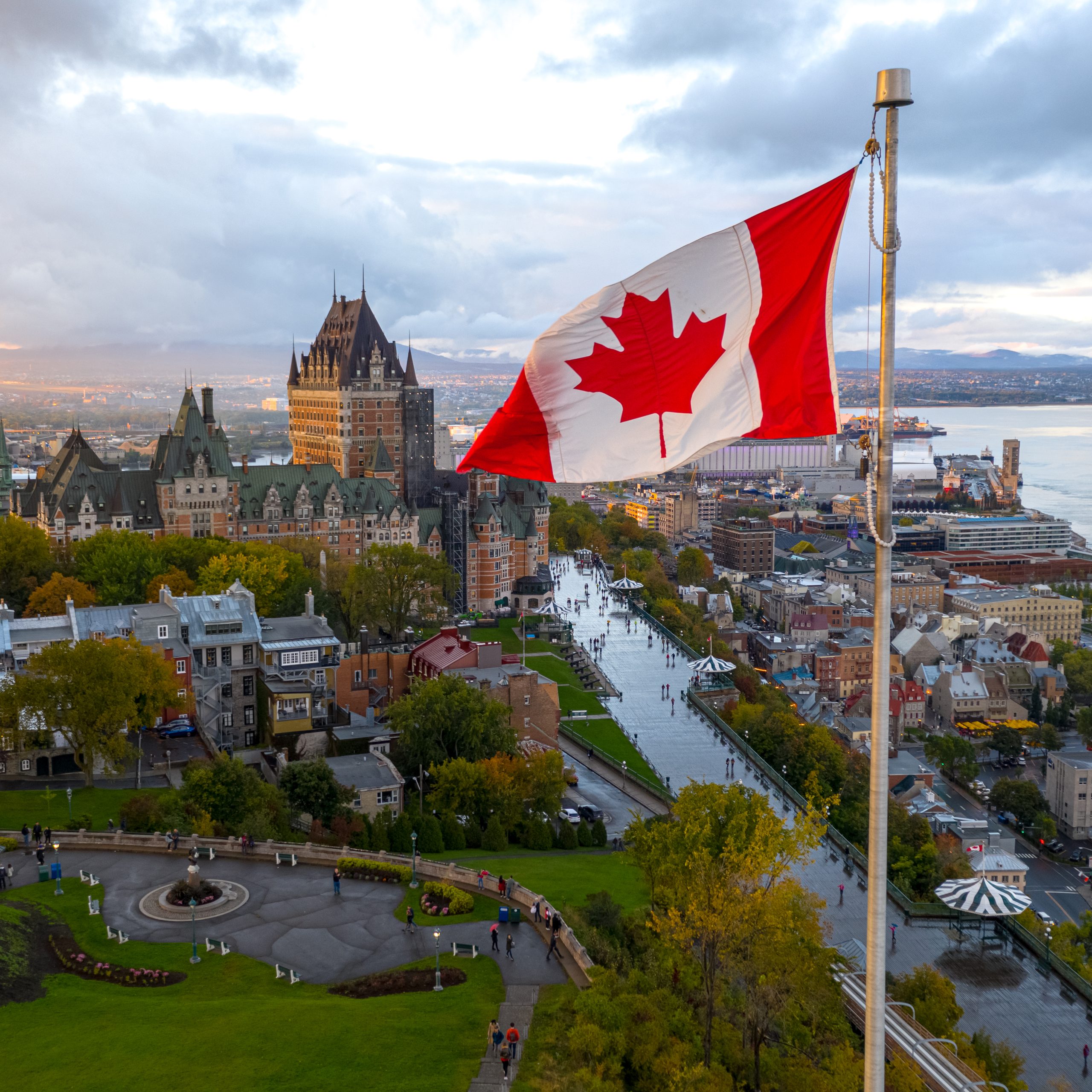 A flowing Canadian flag on a flagpole. Taken at sunset with Old Quebec City and the St. Lawrence River in the background. Aerial HDR view.