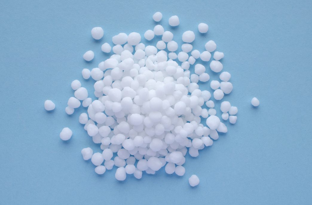 Urea granules on a blue background, space for text, top view. Nitrogen mineral fertilizer - urea. Ammonium nitrate, a salt of ammonia and nitric acid, is used for plant nutrition, top view
