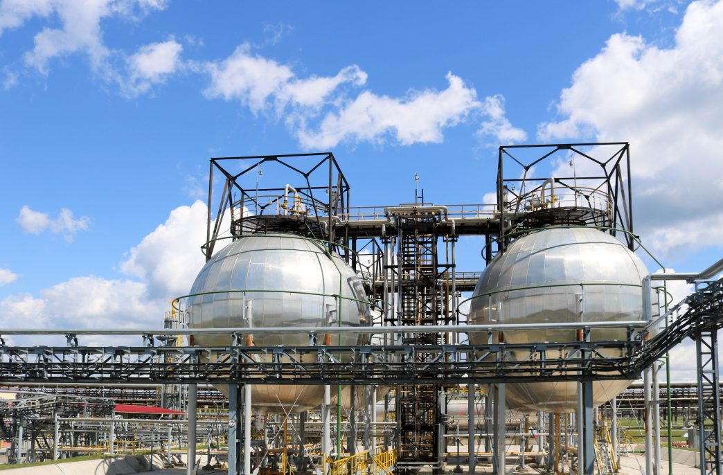 A large round ball-shaped shiny metallic high-pressure iron storage tank for ammonia is strong with pipes and equipment at the petrochemical chemical refinery industrial refinery.