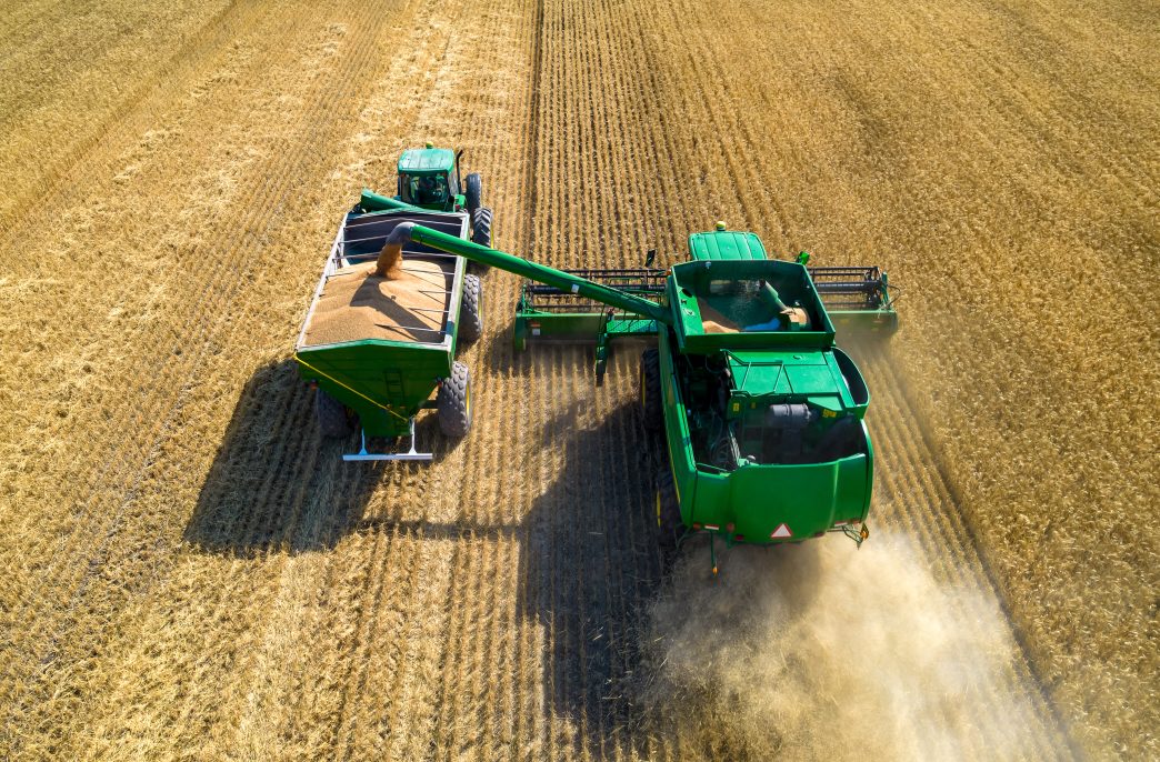 Chaco, Argentina, October 22, 2022: Aerial view of combine harvester unloading grain in cargo trailer working during harvesting season on large ripe wheat field in Argentina.