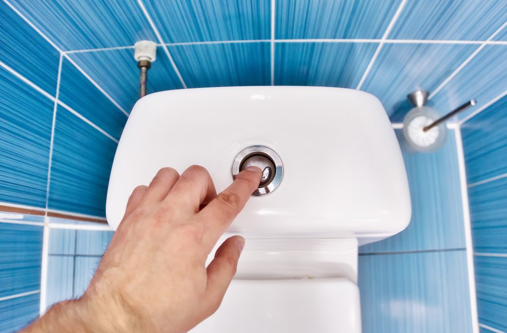 Man presses toilet button with his hand and drains water in toilet. First-person view. Interior space of restroom for men..