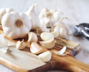 Bulbs of garlic on cutting board and garlic press on light background
